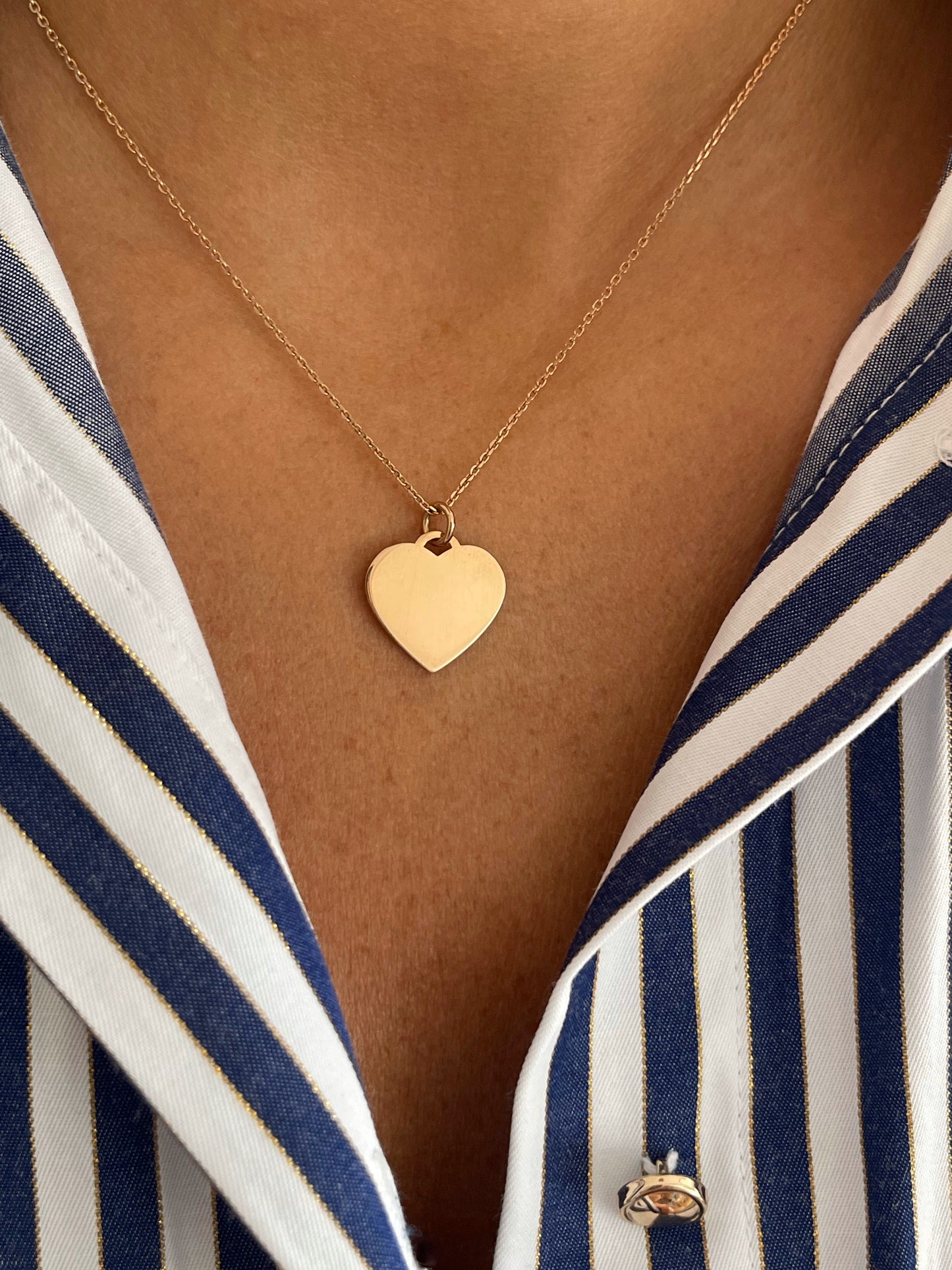 Gold heart-shaped necklace on a person wearing a striped shirt