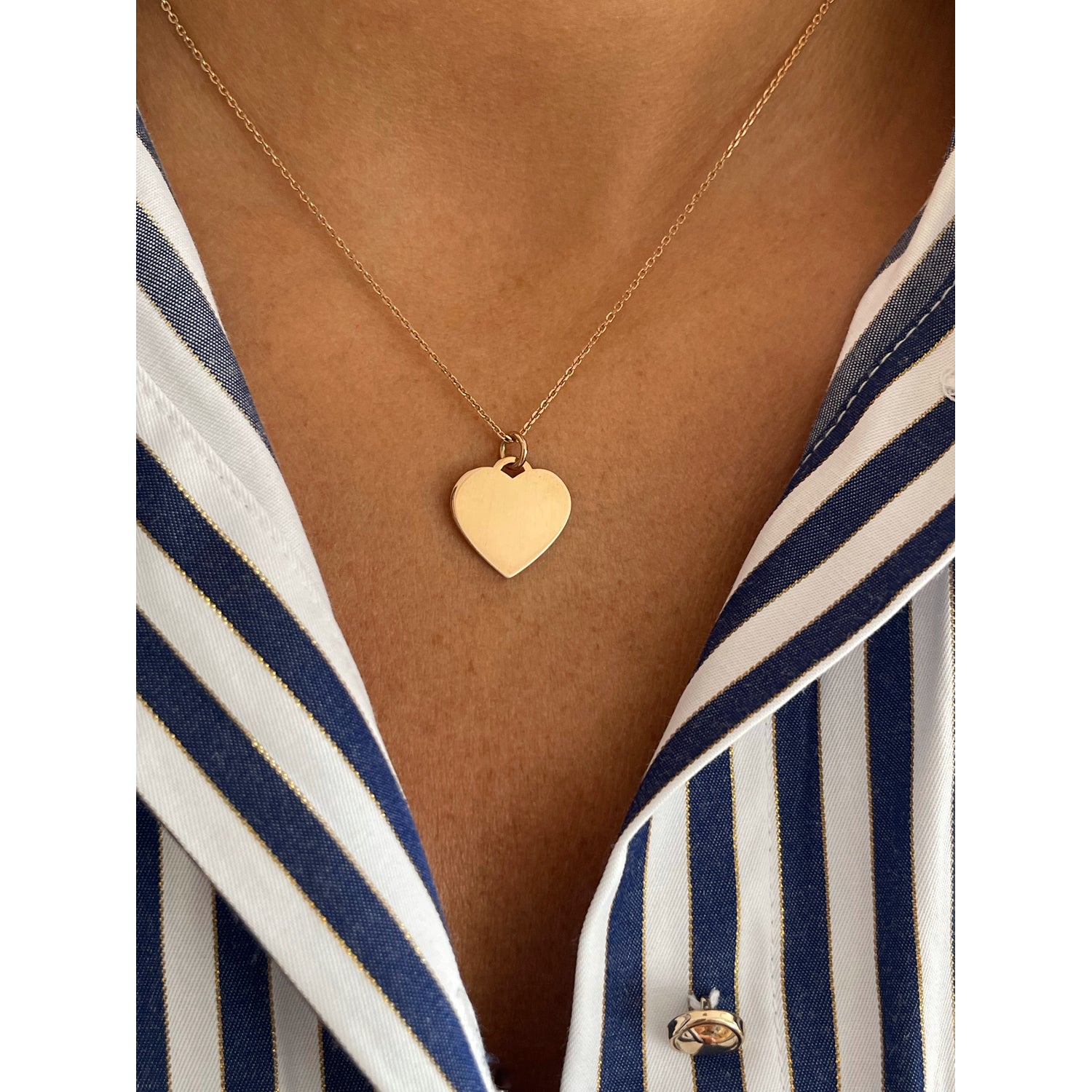 Gold heart-shaped necklace on a person wearing a striped shirt