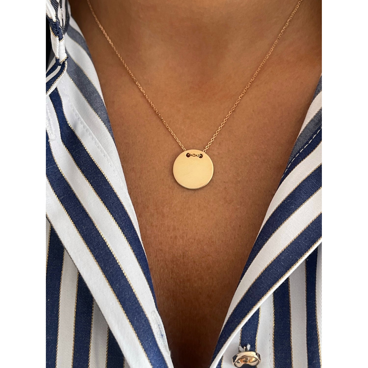 Gold necklace with a round pendant worn by a person in a striped shirt