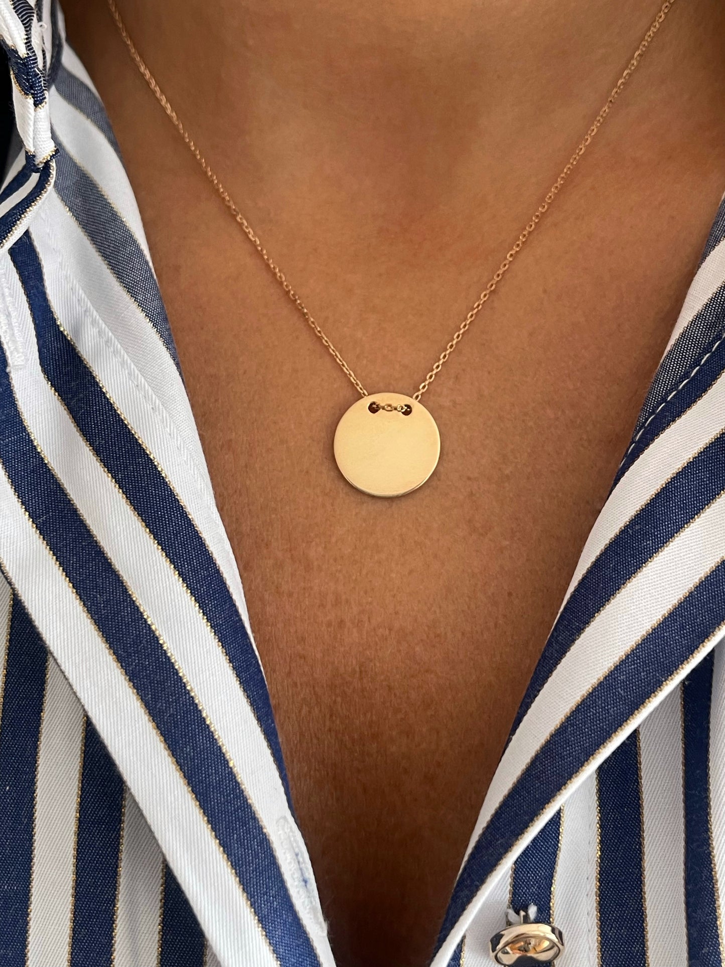 Gold necklace with a round pendant worn by a person in a striped shirt