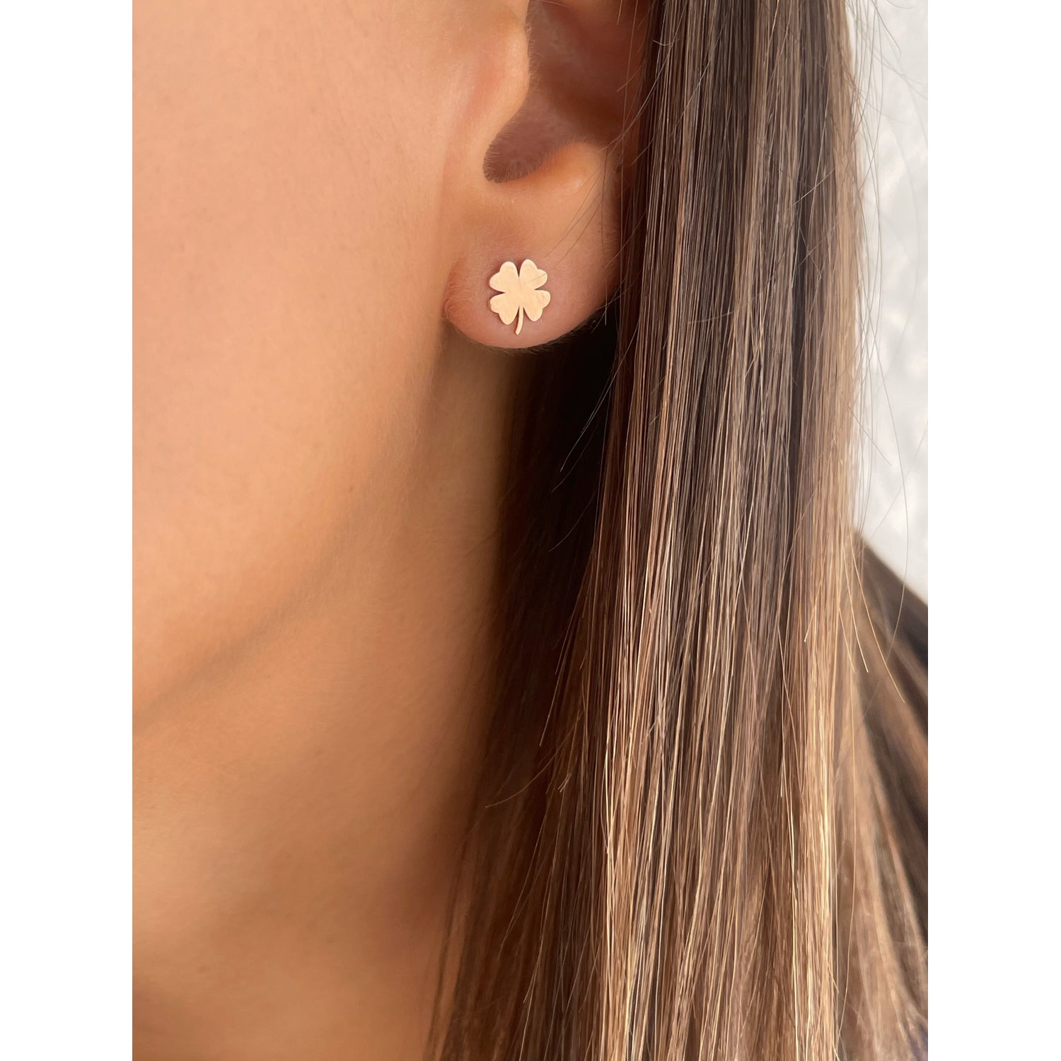 Gold four-leaf clover earrings worn by a person with brown hair.