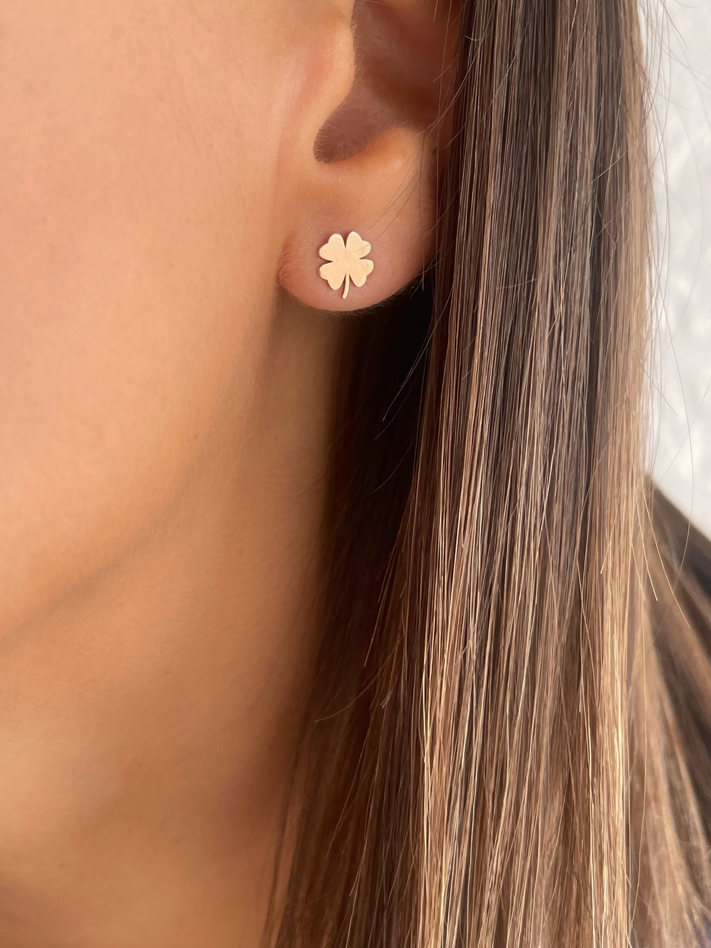 Gold four-leaf clover earrings worn by a person with brown hair.